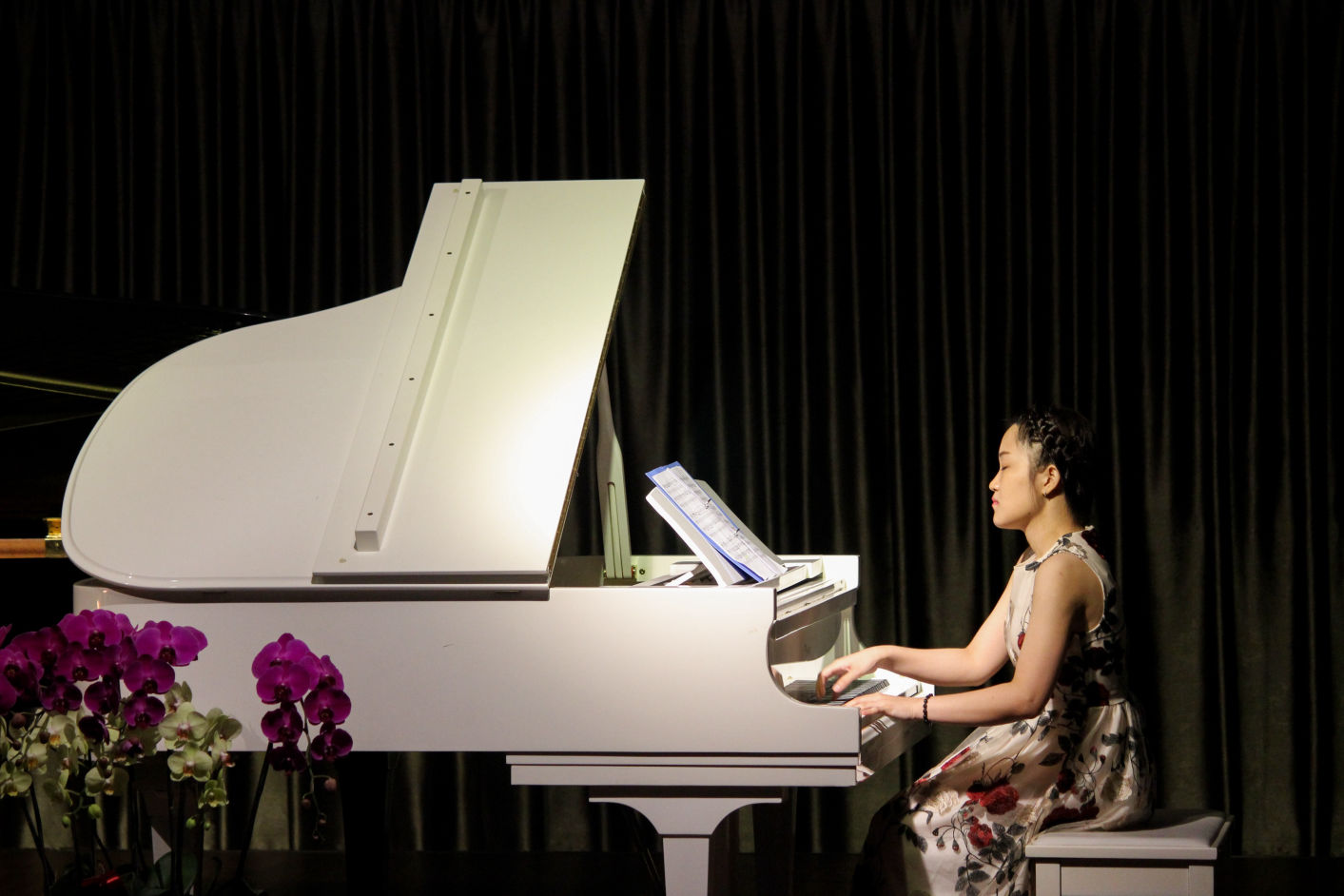A young female student of Maria Drost's sings and plays a white piano at the Music School's annual Singing Academy Showcase