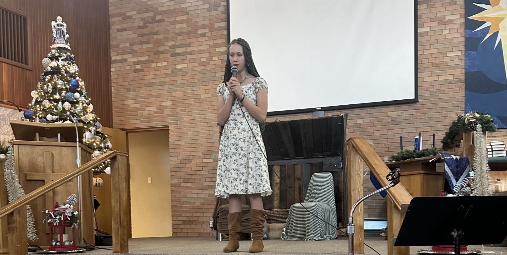 A young female student of Maria Drost's wearing a white flower dress is singing her heart out at the Music School's annual Christmas Showcase
